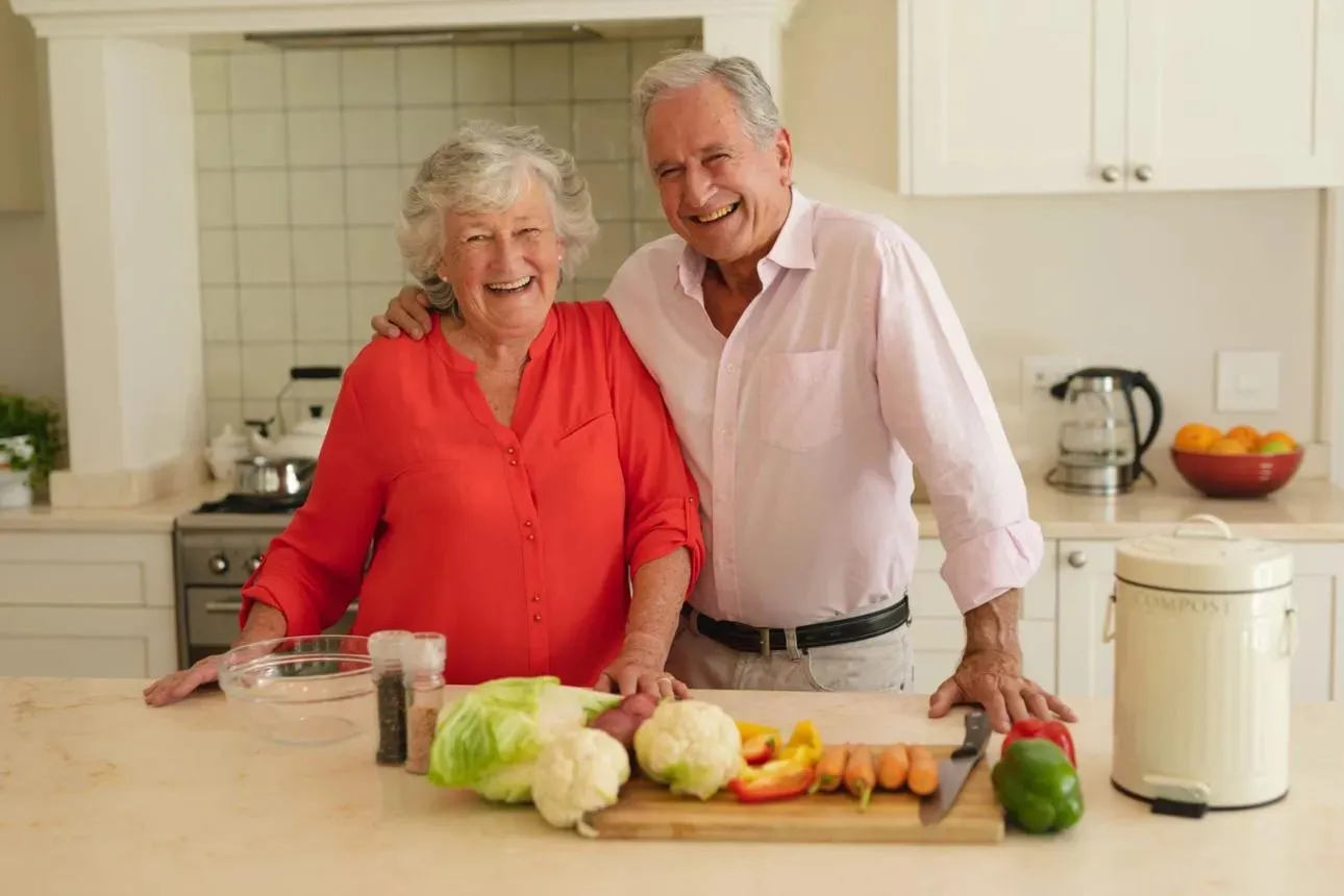 'Close-up portrait of a smiling middle-aged or senior couple leaning close to each other, with the woman on the left in a beige sweater and the man on the right in a blue shirt.'